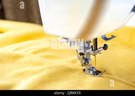 Moderner Nähmaschinenpresser-Fuß mit gelbem Stoff und Faden, Nahaufnahme, Kopierraum. Nähprozess Kleidung, Vorhänge, Polster. Unternehmen, Hobby, Stockfoto