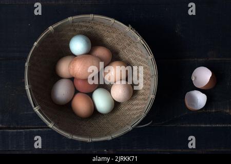Von oben Schuss Korbschale mit rohen Eiern auf Holztisch mit Eierschale in der Nähe gefüllt Stockfoto