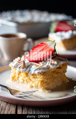 Süßer, köstlicher Kuchen aus drei Milchsorten mit halbfrischer Erdbeere auf weißem Teller auf Holztisch Stockfoto