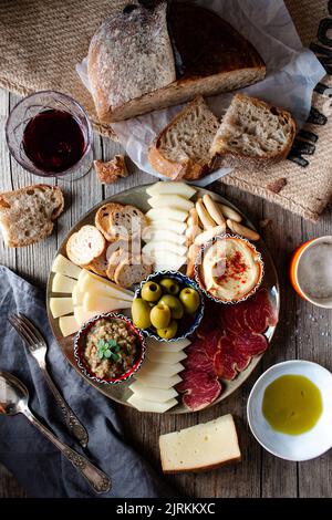 Von oben appetitliche Snackplatte mit mehreren Sorten Käse, Oliven, Schweinelende und frisch gebackenem Brot auf Holztisch Stockfoto