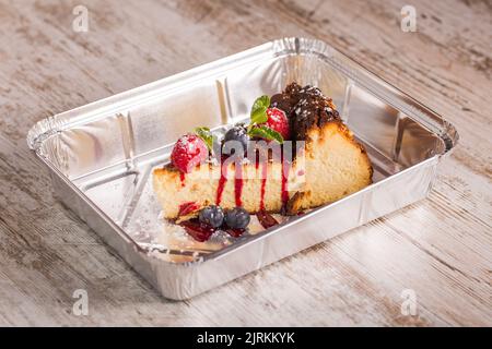 Leckerer Käsekuchen mit roter Marmelade und reifen Himbeeren mit Heidelbeeren in der Nähe von frischen Minzblättern und Puderzucker in der Aluminium-Backform Stockfoto