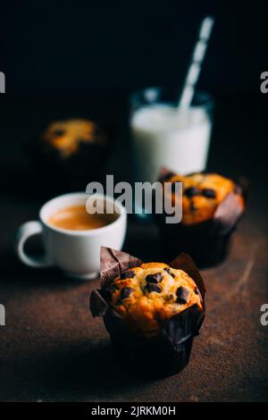 Schokoladen-Muffins, Milch und Kaffeetasse auf dunklem Hintergrund Stockfoto