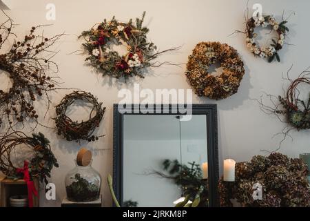 Großer Spiegel mit schwarzem Vintage-Rahmen und angezündete Kerze zwischen wundervollen Kränzen mit rot-weißen und gelben trockenen und grünen frischen Blumen, die mit Bro komponiert sind Stockfoto