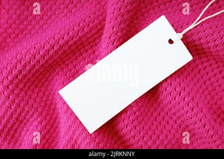 Weiße leere rechteckige Kleidung Tag, Label Mockup Vorlage auf rosa gestrickten Stoff Hintergrund . Preisschild mit Platz für Text. Einkaufen, SA Stockfoto