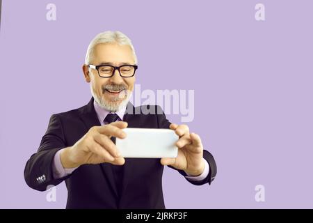 Fröhlicher Geschäftsmann macht Selfie auf Handy auf pastellviolettem Hintergrund. Stockfoto