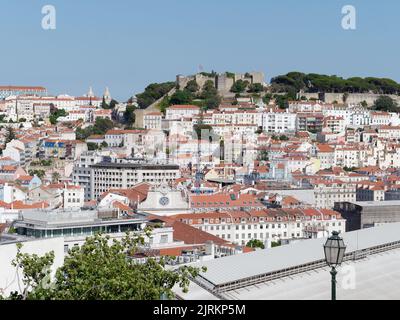 Blick vom Aussichtspunkt (Miradouro) São pedro de Alcântara in Lissabon, Portugal an einem Sommerabend über den Dächern der Stadt. Schloss St. Georges dahinter. Stockfoto