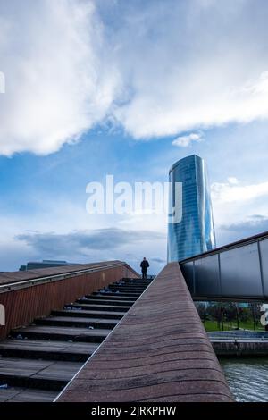 Eine einköpfige Person, die an einem regnerischen Tag eine Treppe hinaufsteigt und zu einem Wolkenkratzer hinaufsteigt, mit vielen Wolken am Himmel. Stockfoto