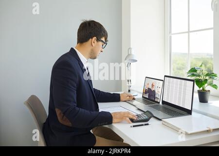 Finanzbuchhalter, der Bürolaptops verwendet, mit Tabellenkalkulationen arbeitet und einen Videoanruf führt Stockfoto