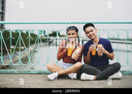 Junges vietnamesisches Paar, das draußen sitzt und Sandwiches und Saft getrunken hat Stockfoto