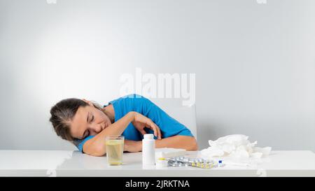 Eine kranke Frau ohne Kraft liegt auf dem Tisch neben den Pillen Stockfoto