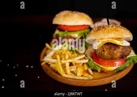 Burger, Hamburger mit Ei oder Cheeseburger mit pommes Frites, Gurken und Zwiebeln auf Holzbrett. Draufsicht. Fast-Food-Konzept Stockfoto