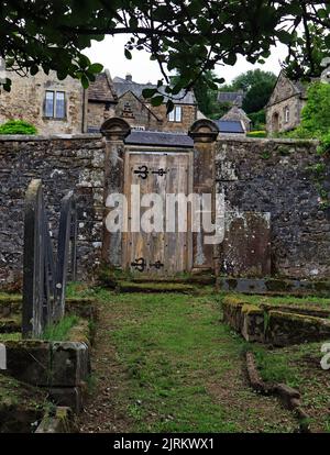 Ein altes, schweres Holztor in der Mauer um den Grabhof der St. John the Baptist Church im malerischen Dorf Winster in Derbyshire Stockfoto