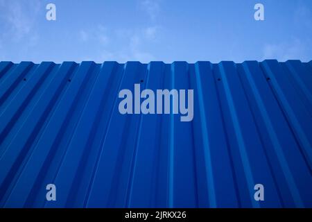 Textur einer metallblau bemalten dunklen Zaun Wand mit einem Himmel im Hintergrund. Stockfoto