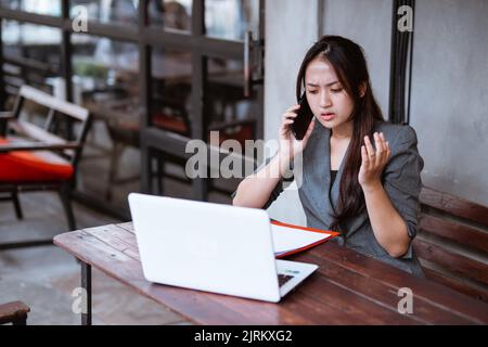 Verwirrt junge Geschäftsfrau, während sie ihr Mobiltelefon während der Arbeit benutzte Stockfoto
