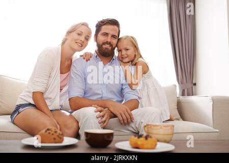 Porträt eines glücklichen Vaters, einer Mutter und einer kleinen Tochter, die sich im Wohnzimmer ausruhen Stockfoto
