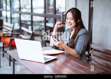 Glücklich aufgeregt junge Geschäftsfrau während der Arbeit und mit ihrem Telefon. Stockfoto