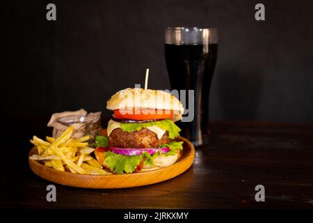 Köstlicher Hamburger mit Cola und Pommes auf einem Holztisch mit dunkelbraunem Hintergrund. Fast-Food-Konzept. Stockfoto