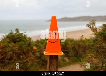 Fröhliches Gesicht oranger Verkehrskegel am Woolacombe Bay Beach, North Devon, England, Großbritannien Stockfoto
