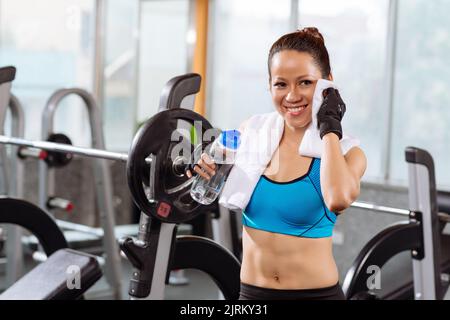 Lächelnde, sportliche junge Frau, die sich nach intensivem Training ins Gesicht wischte Stockfoto