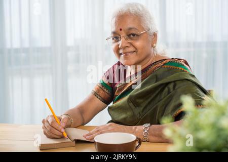 Ältere indische Frau, die am Tisch sitzt und ihr Tagebuch schreibt Stockfoto