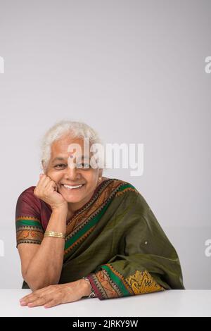 Fröhliche alte Indina-Frau mit Binde, die sich auf den Tisch lehnte und die Kamera ansah Stockfoto