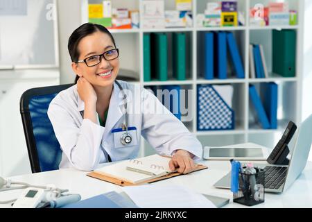 Ziemlich lächelnde vietnamesische Ärztin an ihrem Tisch Stockfoto