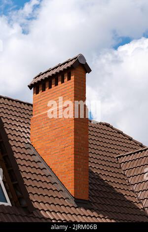 Nahaufnahme eines Schornsteins auf einem Schindeldach aus Metallziegel gegen den blauen Himmel mit Wolken. Stockfoto