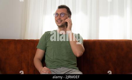 Ein Mann sitzt auf der Couch und spricht zu Hause am Telefon Stockfoto