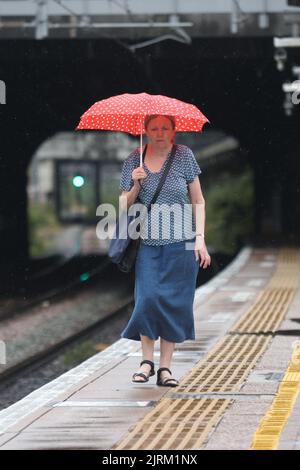 Eine Frau benutzt einen Regenschirm, wenn sie die Plattform der Ealing Broadway Station im Westen Londons hinuntergeht, da das Met Office eine gelbe Warnung für Gewitter und heftigen Regen in Süd- und Ostengland ausgegeben hat, wobei die Fahrbedingungen möglicherweise von Spray, stehendem Wasser und sogar Hagel beeinflusst werden, Sowie mögliche Verspätungen der Zugdienste, Stromausfälle, Überschwemmungen und Blitzeinschläge. Bilddatum: Donnerstag, 25. August 2022. Stockfoto