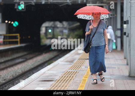 Eine Frau benutzt einen Regenschirm, wenn sie die Plattform der Ealing Broadway Station im Westen Londons hinuntergeht, da das Met Office eine gelbe Warnung für Gewitter und heftigen Regen in Süd- und Ostengland ausgegeben hat, wobei die Fahrbedingungen möglicherweise von Spray, stehendem Wasser und sogar Hagel beeinflusst werden, Sowie mögliche Verspätungen der Zugdienste, Stromausfälle, Überschwemmungen und Blitzeinschläge. Bilddatum: Donnerstag, 25. August 2022. Stockfoto