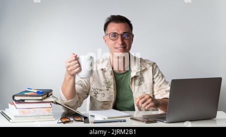 Ein junger Mann in stilvoller Kleidung trinkt Kaffee an seinem Schreibtisch - Hipster Stockfoto