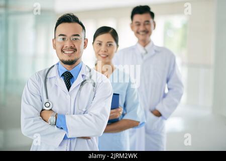 Fröhlicher vietnamesisch-Praktizierender und seine Mitarbeiter stehen dahinter Stockfoto