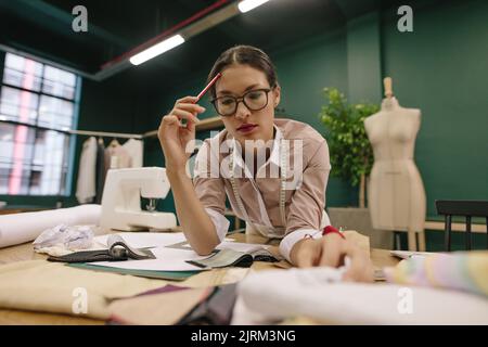 Weibliche Modedesignerin im Studio Wahl Stoff für Kleid. Schneiderin, die in ihrem Studio arbeitet und über die Stoffauswahl nachdenkt. Stockfoto