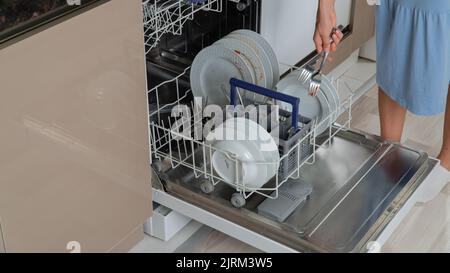 Eine Frau stellt schmutziges Besteck in den Geschirrspüler Stockfoto