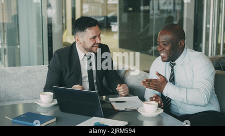 Zwei Geschäftsleute, die sich im modernen Café unterhalten und lachen. Männer haben Spaß und scherzen Blick auf Laptop-Computer während der Kaffeepause Stockfoto