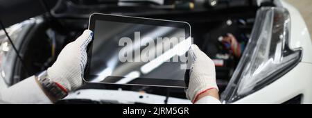 Meister der Werkstatt, der das digitale Tablet in der Nähe der geöffneten Motorhaube der Nahaufnahme des Autos hält Stockfoto