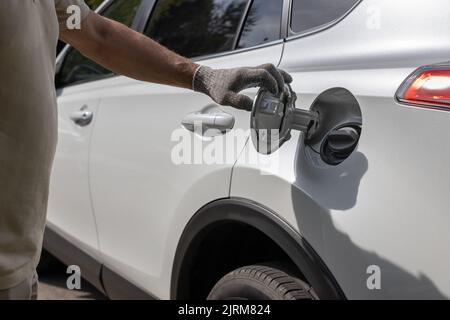 Der Mann öffnet die Luke des Gastanks des Autos. Mit Handschuhen geriebte Hand öffnet den Gastank Stockfoto