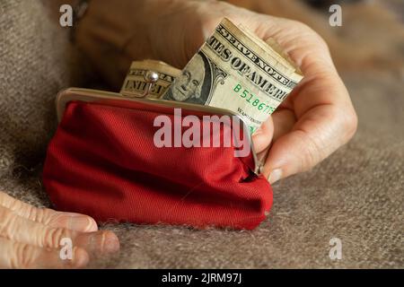 Die Hände einer alten Frau nehmen eine Dollarnote aus einer weichen roten Brieftasche, Geld in einer Brieftasche, Finanzen Stockfoto