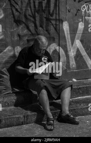 Neapel, Italien - 26. Juli 2022: Porträt eines alten Mannes, der ein Buch über die Treppe liest. Stockfoto