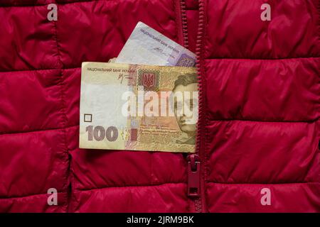 Ukrainisches Geld hundertfünfzig Griwna, die aus der Tasche einer roten Jacke ragen, ukrainisches Geld, Finanzen Stockfoto