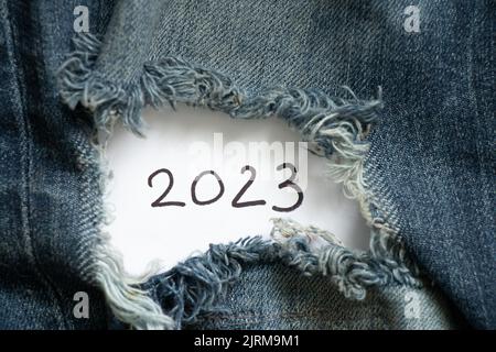 2023 geschrieben auf Papier, das auf zerrissenen Jeans liegt, glückliches neues Jahr 2023, Urlaub und Mode Stockfoto