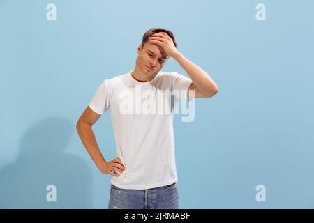 Porträt eines jungen Mannes, der die Handfläche auf der Stirn hält und isoliert auf blauem Studiohintergrund posiert Stockfoto