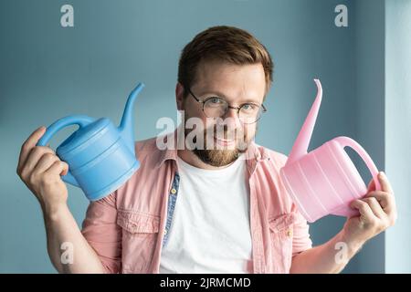 Vater hält zwei Gießkannen für Kinder in den Händen, rosa und blau, er lädt das Kind ein, eine Wahl zu treffen und eine Sache zu nehmen. Stockfoto