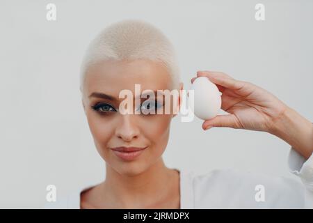 Porträt einer jungen lächelnden, tausendjährigen europäischen Kurzhaarigen Frau, die das Ei in der Hand hält. Schöne glücklich blonde Mädchen im Freien. Stockfoto