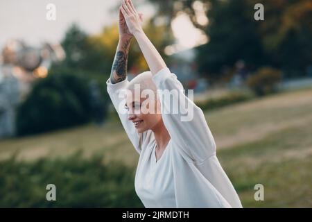 Porträt einer jungen, lächelnden, tausendjährigen europäischen Kurzhaarigen, die im Park Yoga macht. Schöne glücklich blonde Mädchen im Freien. Stockfoto