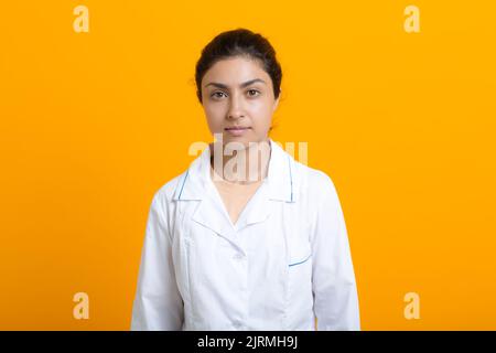 Porträt der indischen Ärztin in weißem medizinischen Kleid isoliert auf gelbem Hintergrund. Stockfoto