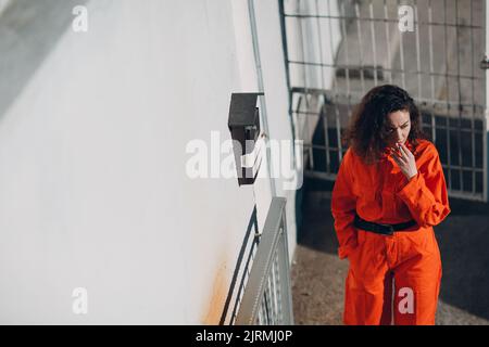 Junge Gefangene Frau in orange Klage im Gefängnis Rauchen. Weiblich in bunten Overalls Porträt Stockfoto