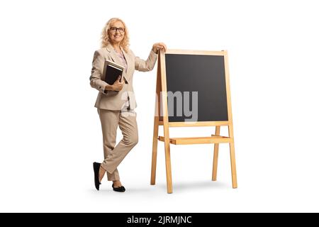In voller Länge Porträt einer Lehrerin, die Bücher hält und neben einer Tafel steht, isoliert auf weißem Hintergrund Stockfoto
