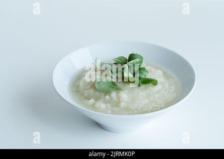 Gesunde vegane Blumenkohlcremesuppe mit Kräutern in weißer Schüssel auf weißem Tisch, Nahaufnahme Stockfoto