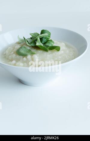 Gesunde vegane Blumenkohlcremesuppe mit Kräutern in weißer Schüssel auf weißem Tisch, Nahaufnahme Stockfoto